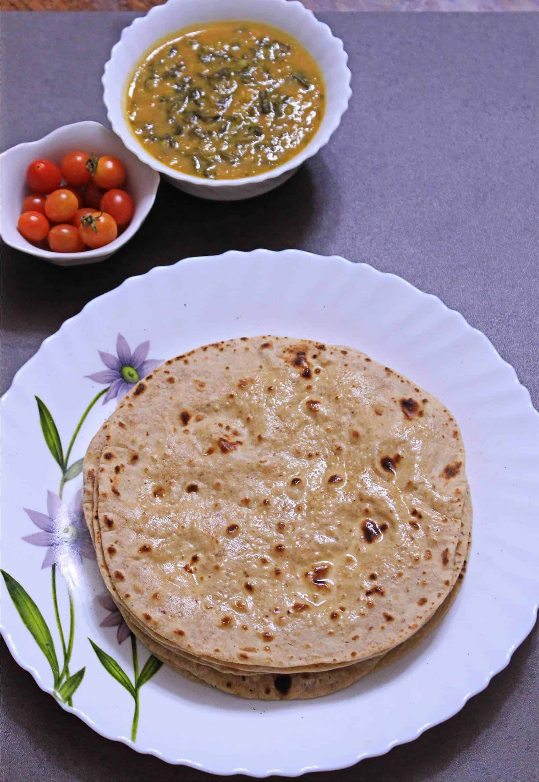 Whole Wheat Phulka | Pulka | Roti Whole Wheat Phulka in a white plate with subzi and tomatoes on the side.